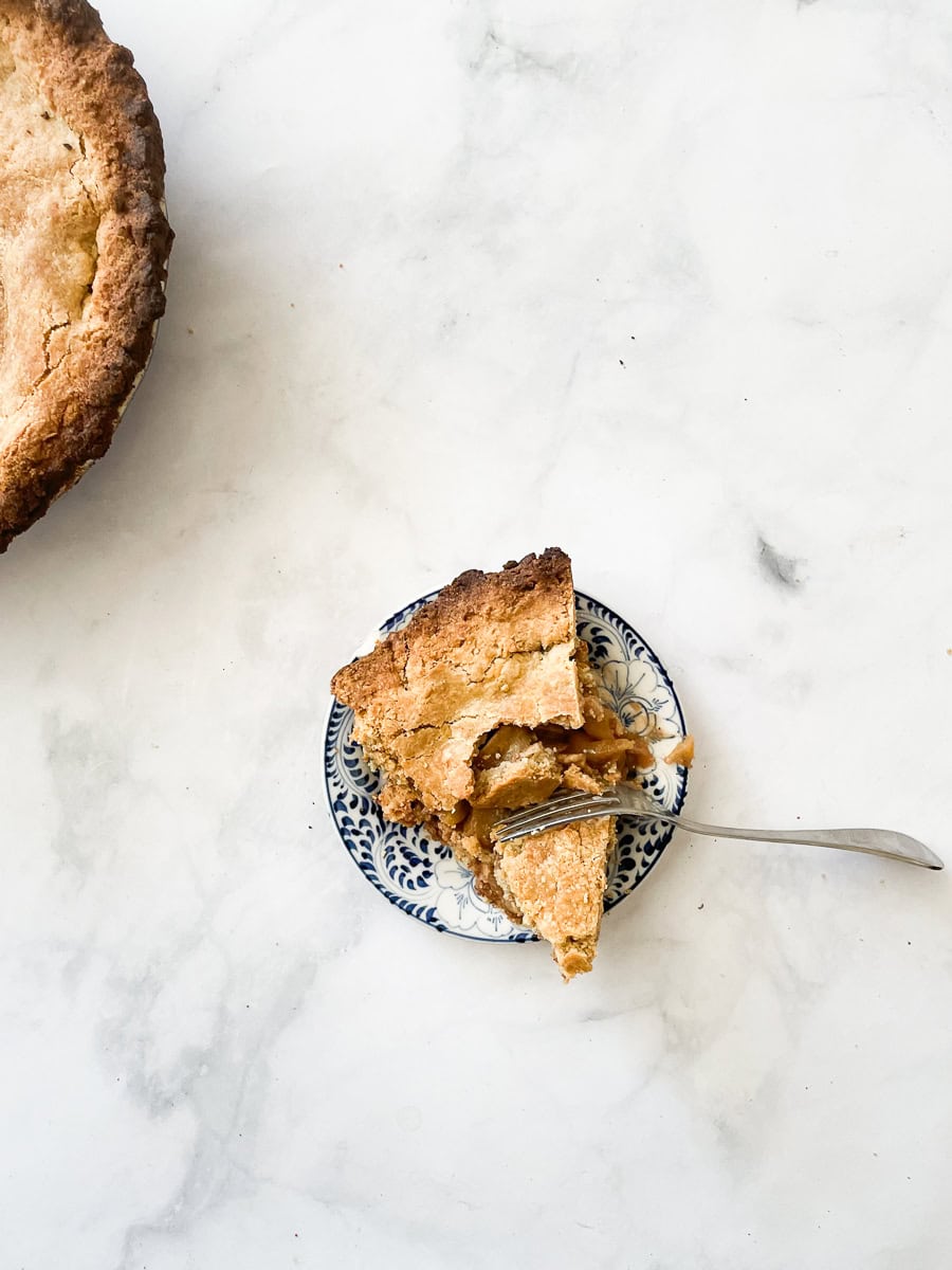 A piece of gluten free apple pie with a fork cutting in on a plate, with the pie to the left.