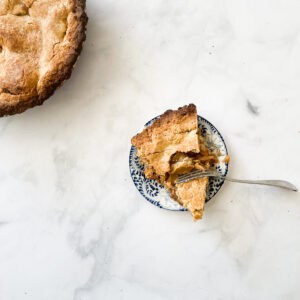 A piece of gluten free apple pie with a fork cutting in on a plate, with the pie to the left.