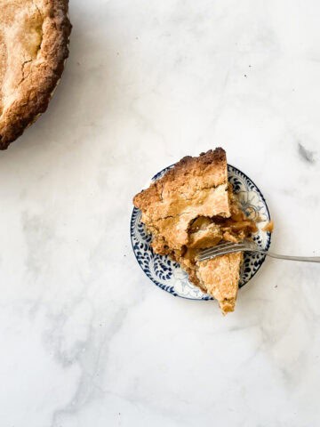 A piece of gluten free apple pie with a fork cutting in on a plate, with the pie to the left.