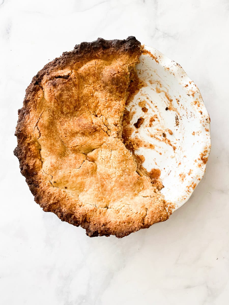 A pie pan with gluten free apple pie with slices cut out.