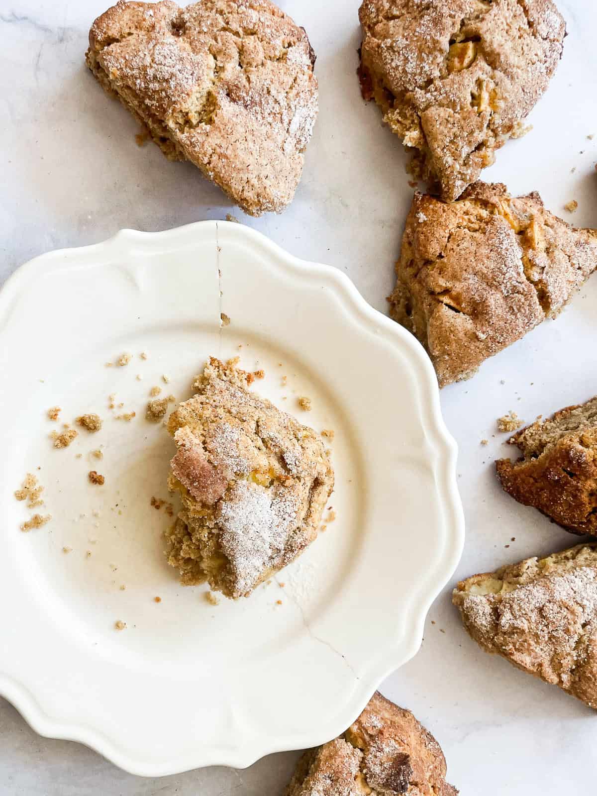 An apple scone on a plate surrounded by more scones.