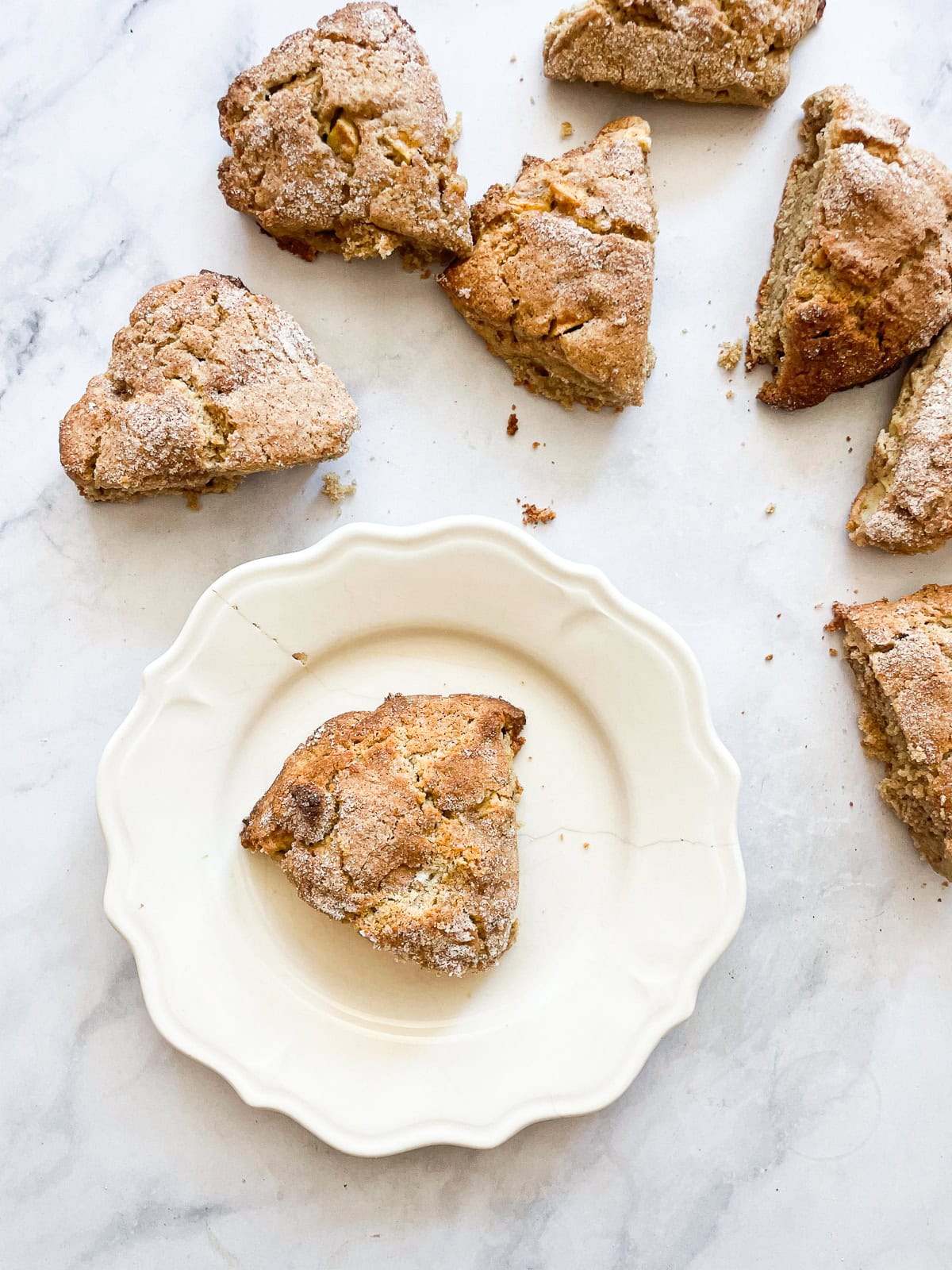 An apple scone on a plate surrounded by more scones.