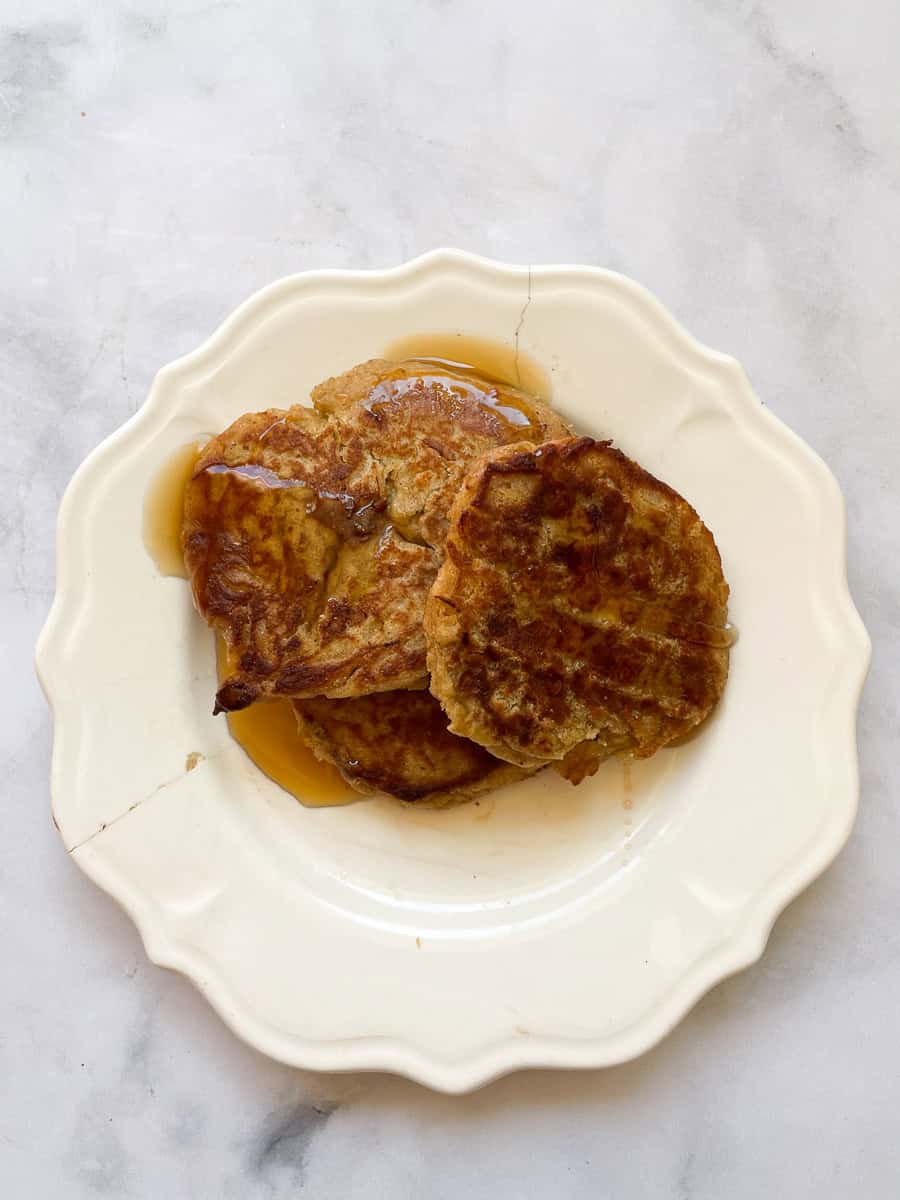 A white plate with gluten free banana buttermilk pancakes and syrup.