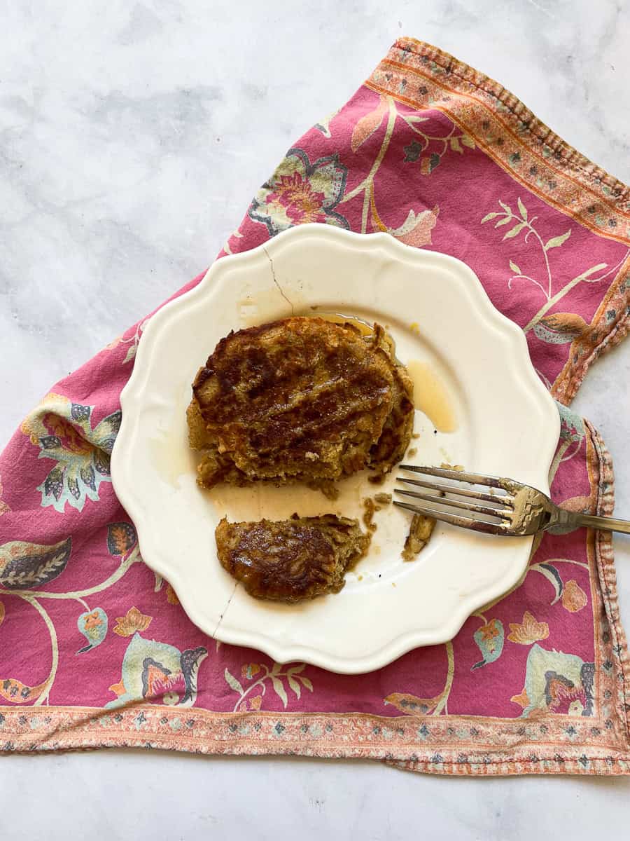 A plate of gluten free banana buttermilk pancakes on top of a pink napkin and a fork on its edge.