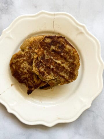 A white plate with gluten free banana buttermilk pancakes and syrup.