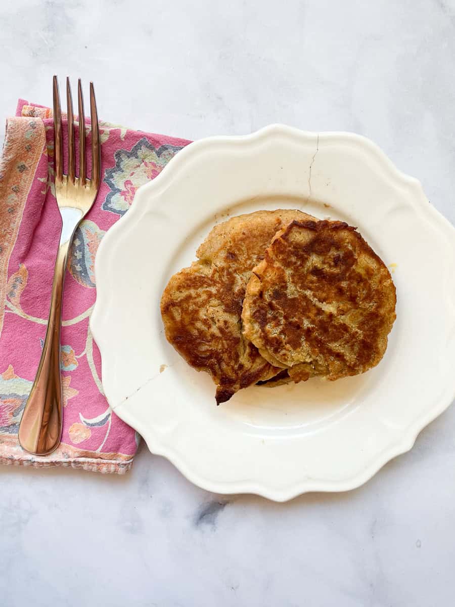 A plate with gluten free banana buttermilk pancakes, a pink napkin, and a fork.