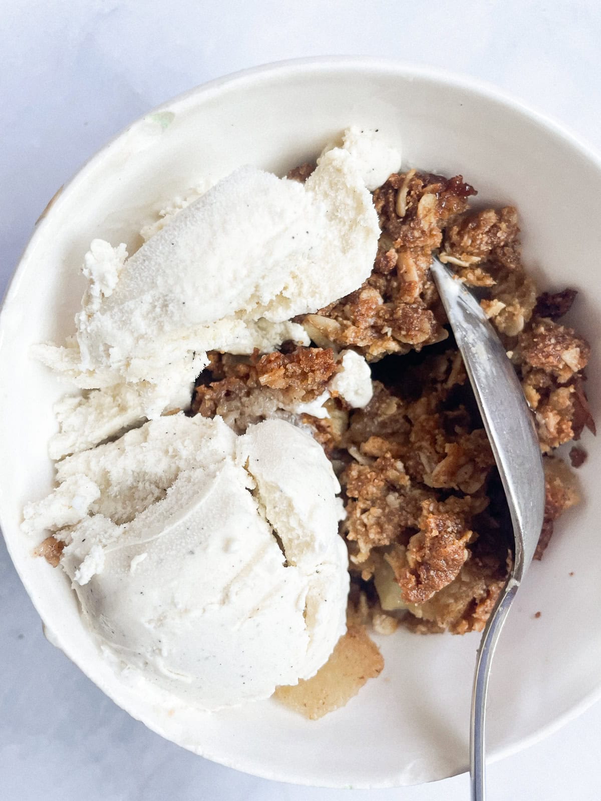 A spoon in a bowl of apple crisp with ice cream.