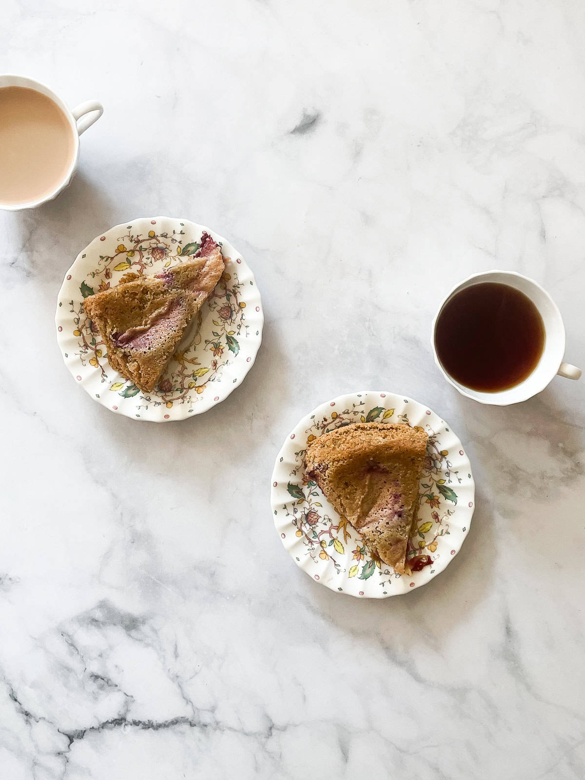 Slices of plum torte on plates with cups of tea.