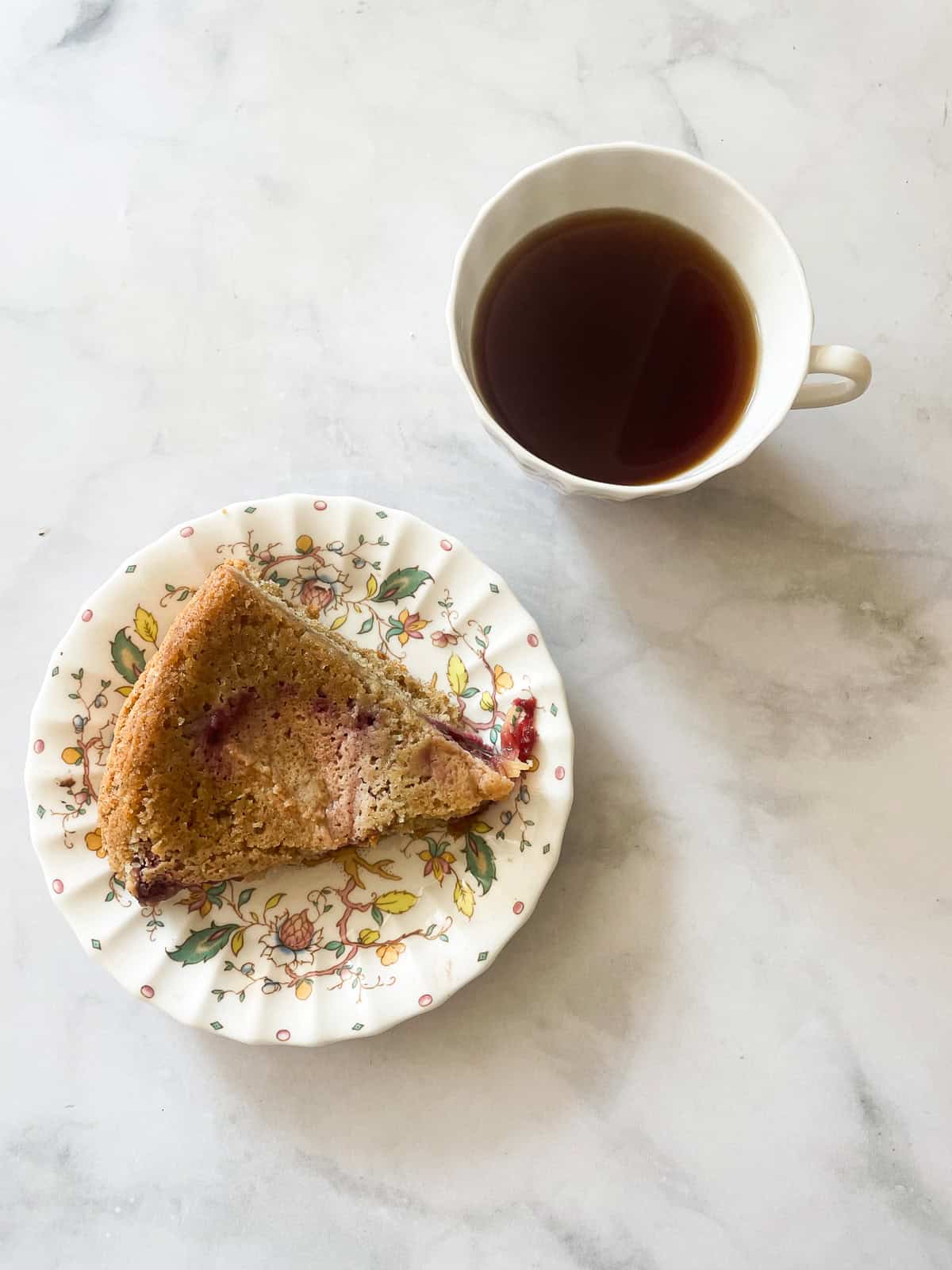 A slice of plum torte on a small plate with a cup of tea.