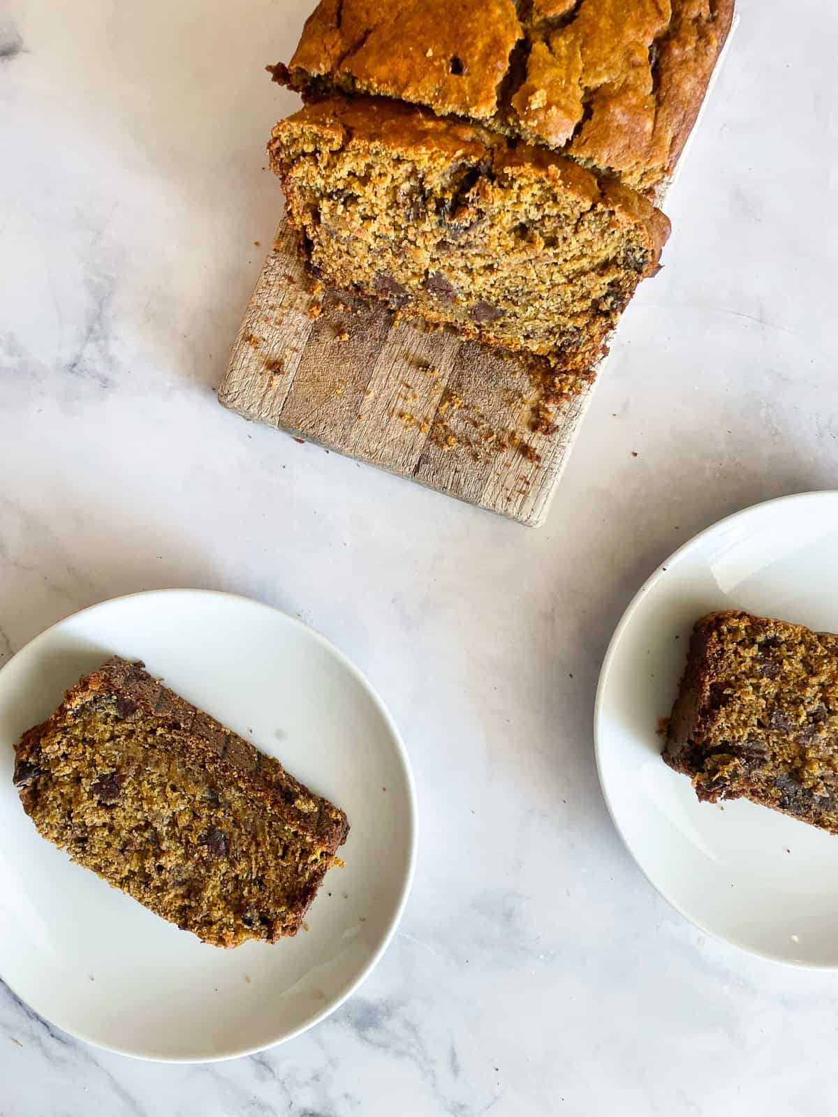 Two slices of pumpkin banana bread on plates next to the loaf.