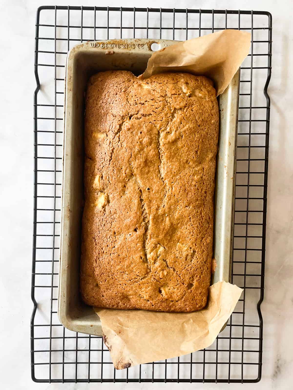 A baked loaf of apple cinnamon bread cools on a rack.