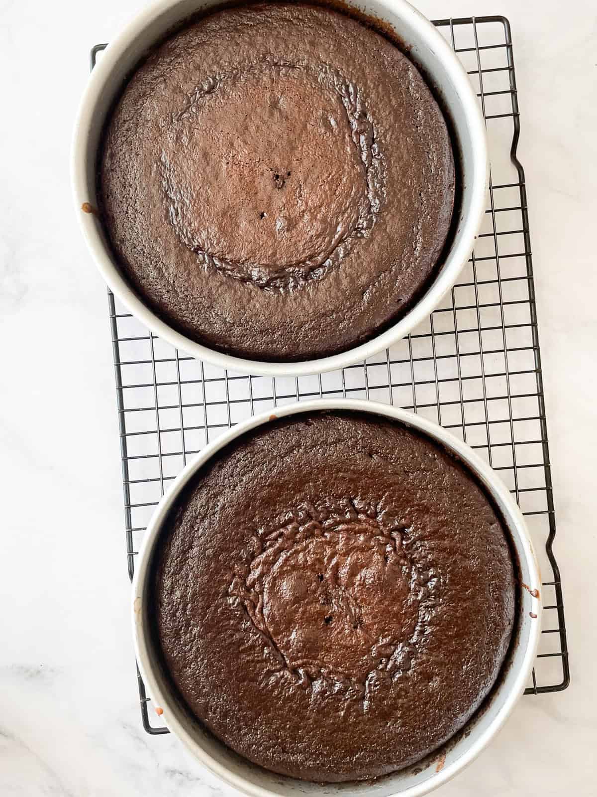 Two rounds of chocolate layer cake cool in pans.