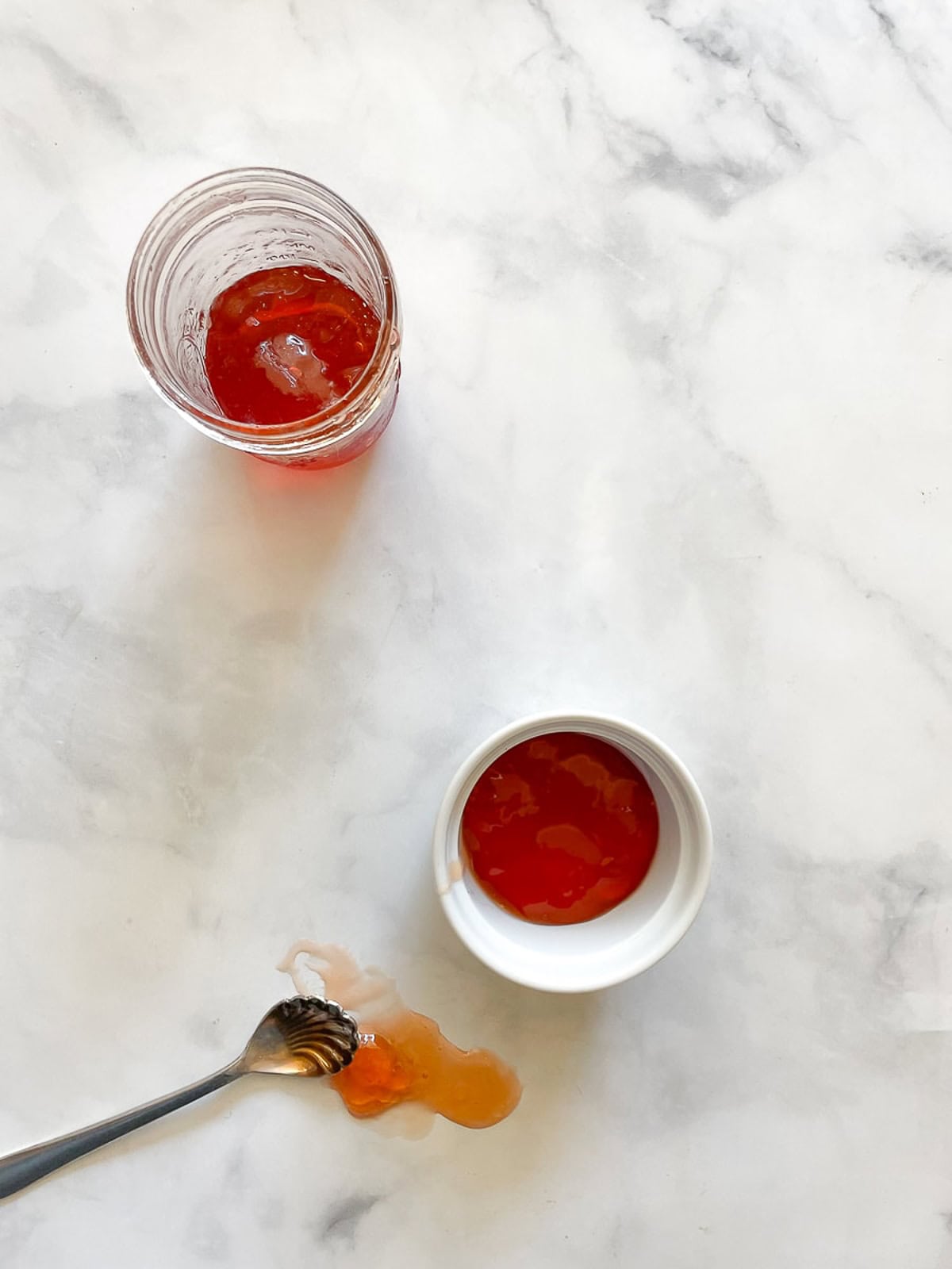 Apple jelly in a jar, dish, and on a counter with a spoon.