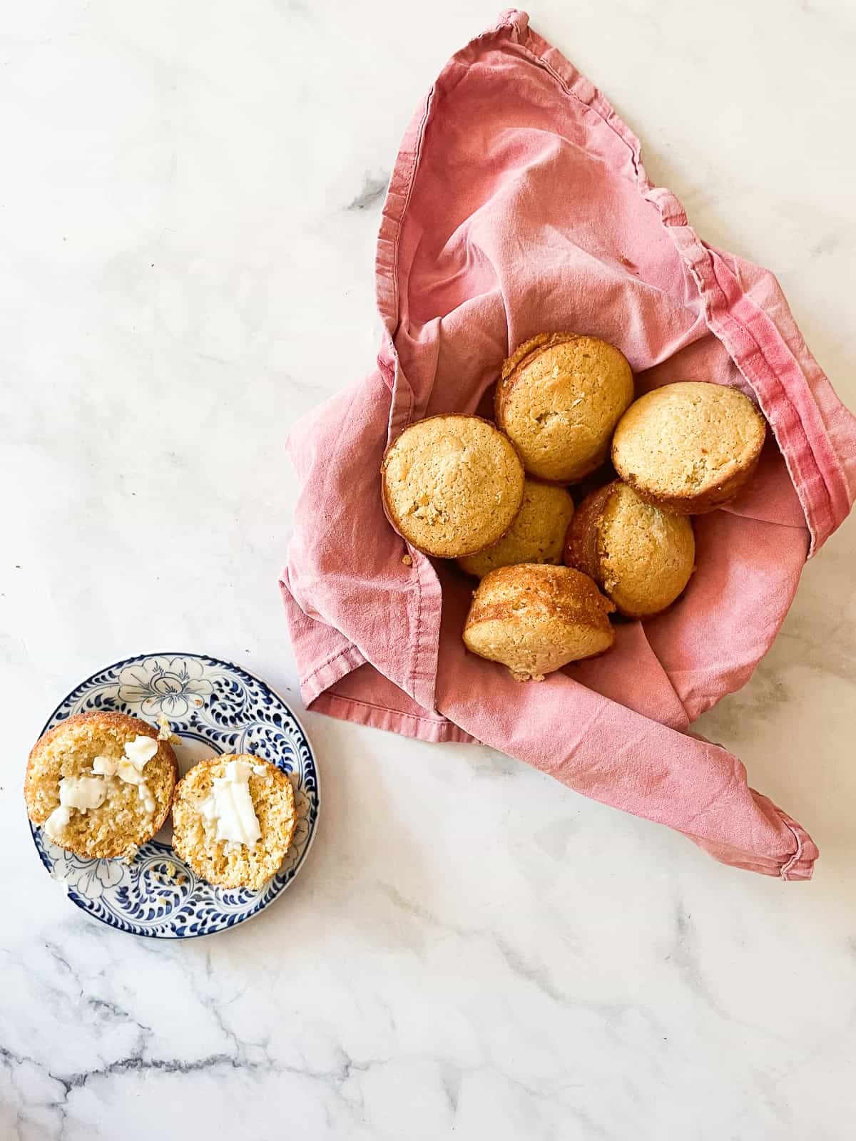 A honey cornbread muffin with butter on a plate next to a basket of muffins.