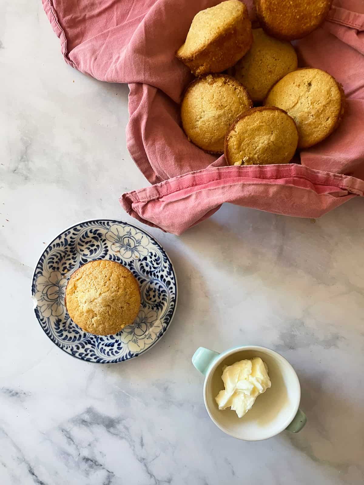 A basket of gluten free honey cornbread muffins in a red napkin with one on a palte.