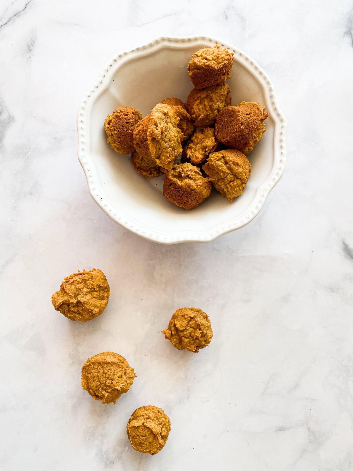 A bowl of gluten free mini pumpkin muffins and muffins next to it.