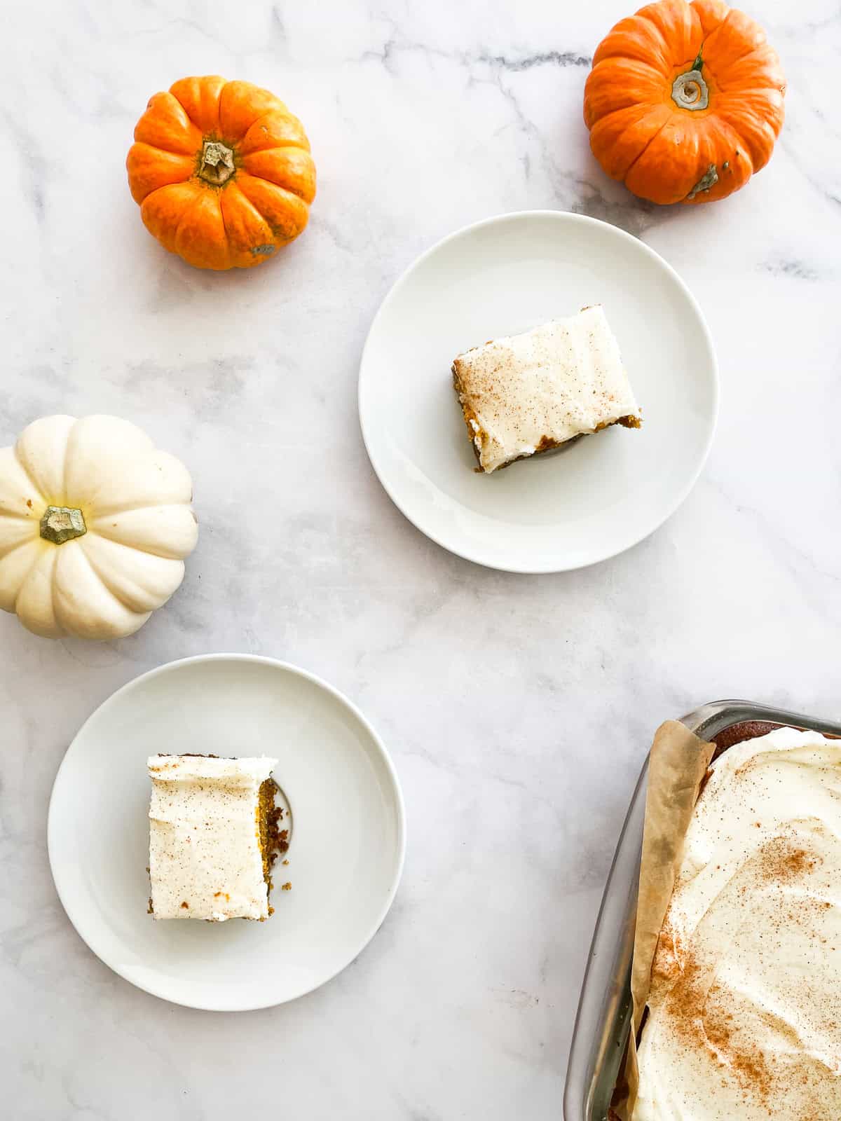 Two gluten free pumpkin bars on plates with mini pumpkins.