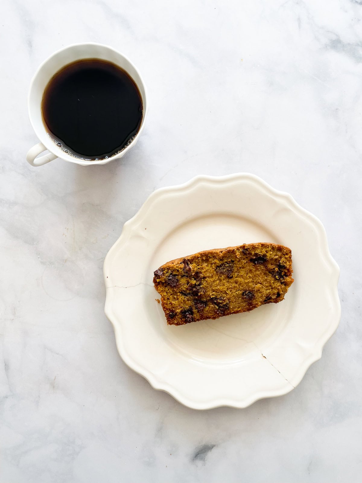 A slice of pumpkin chocolate chip bread on a white plate and a cup of coffee.