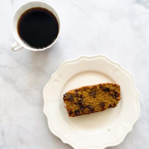 A slice of pumpkin chocolate chip bread on a white plate and a cup of coffee.