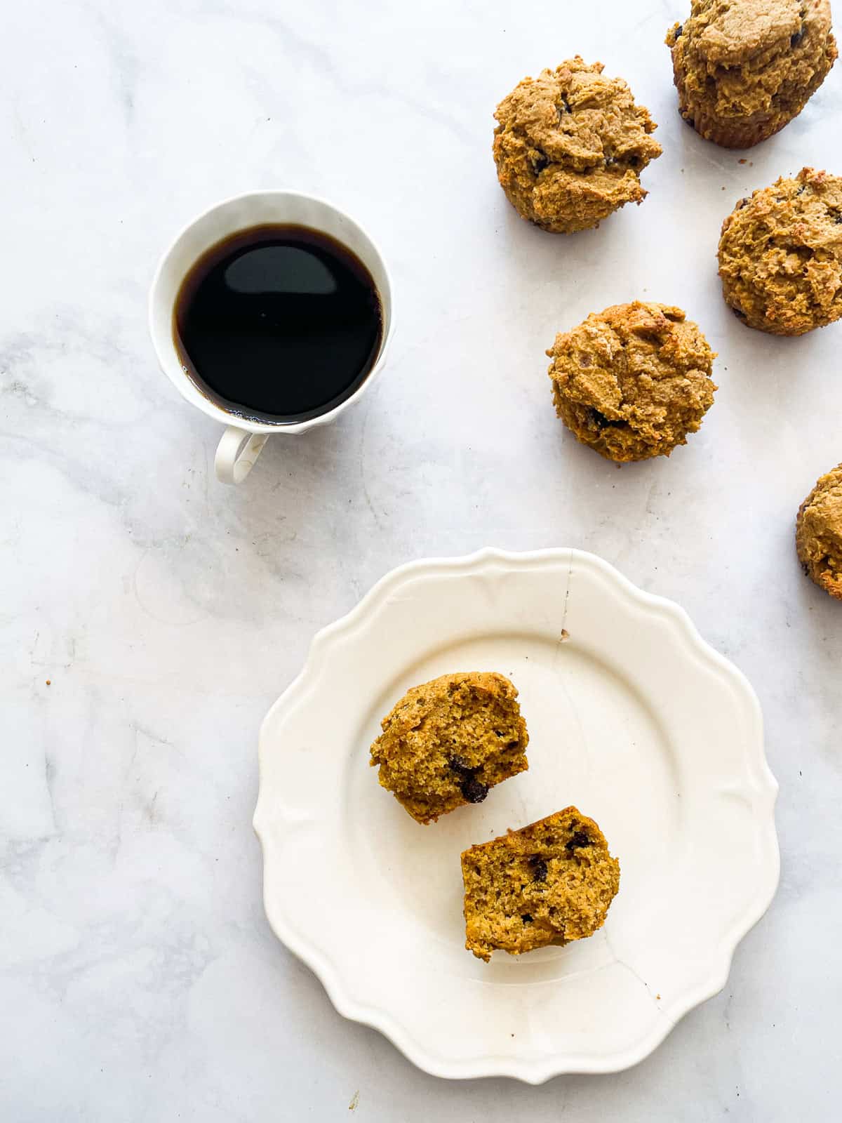 A cup of coffee and pumpkin chocolate chip muffins, one on a plate.