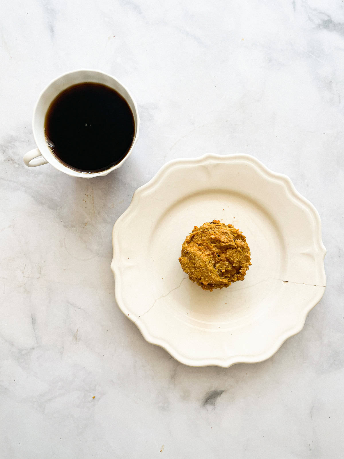 A pumpkin chocolate chip muffin on a plate with a cup of coffee.