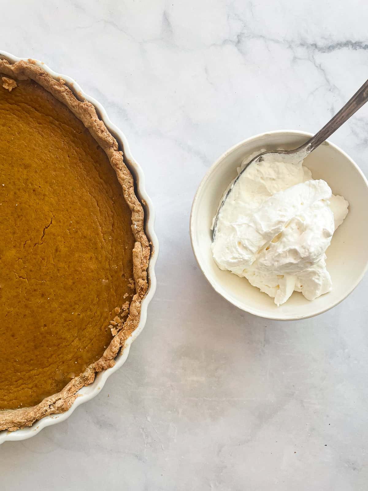 A gluten free pumpkin pie and a bowl of whipped cream.