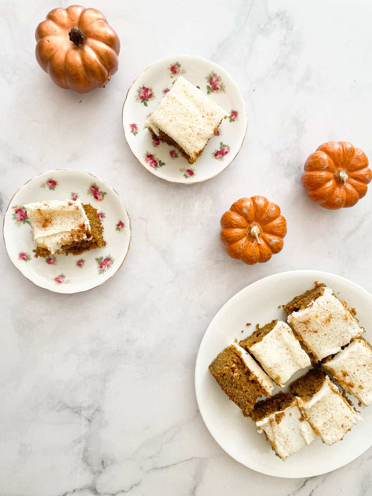 Squares of gluten free pumpkin sheet cake on plates with mini pumpkins.