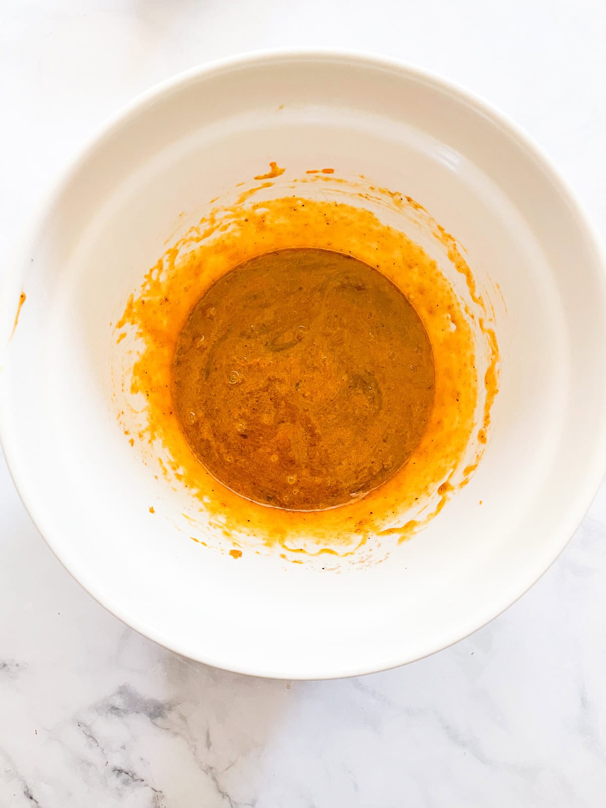 Eggs, melted butter, and pumpkin puree in a bowl.