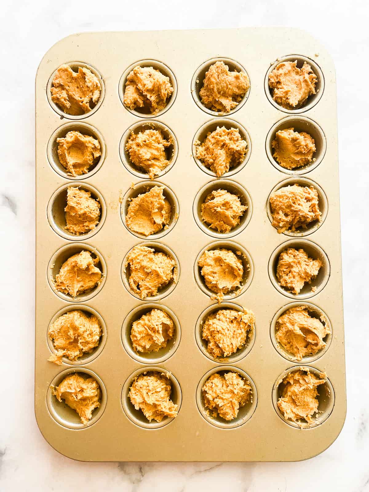 A mini muffin tin full of gluten free mini pumpkin muffin batter.