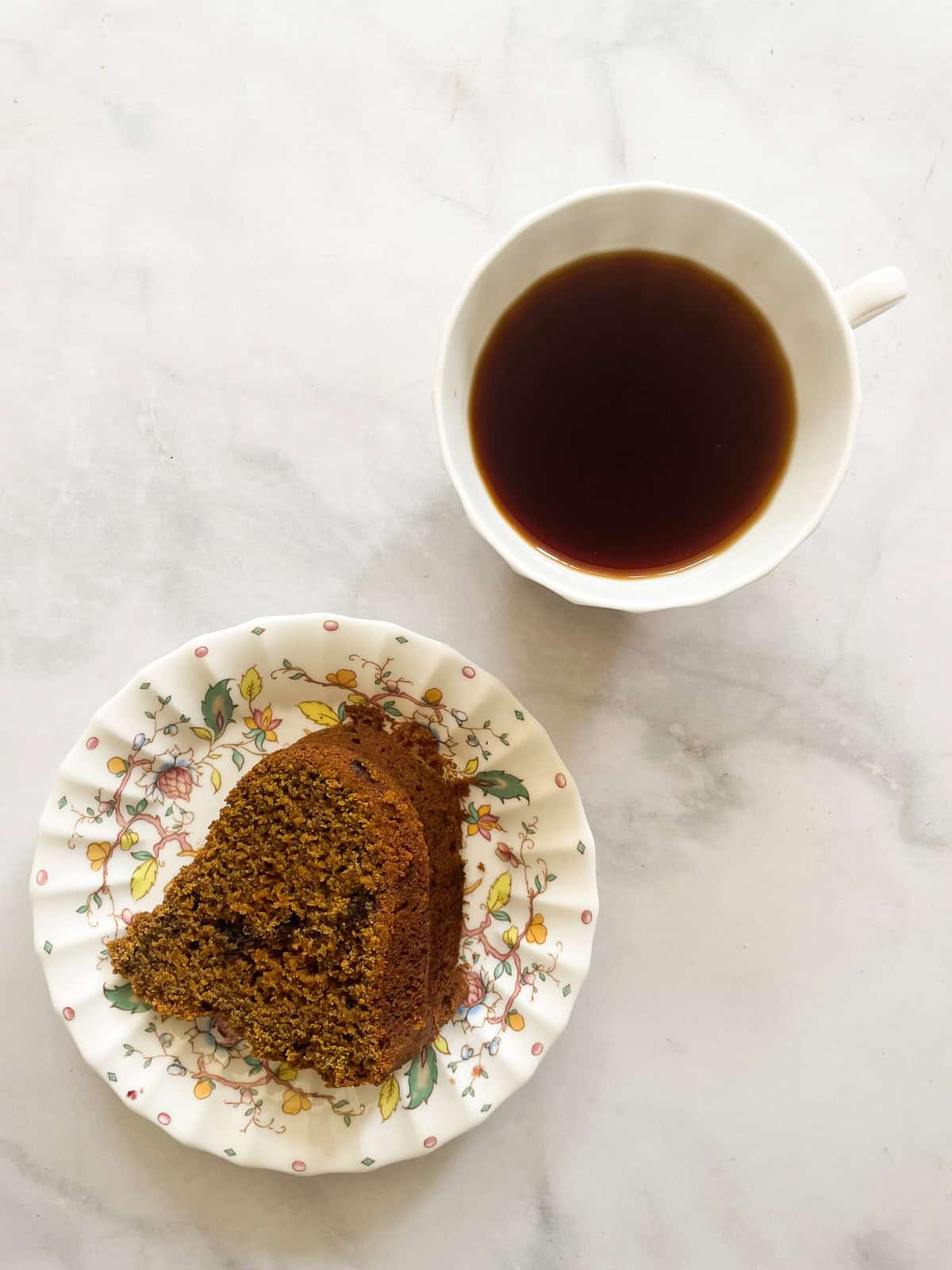 A piece of pumpkin spice cake on a plate with a cup of tea.