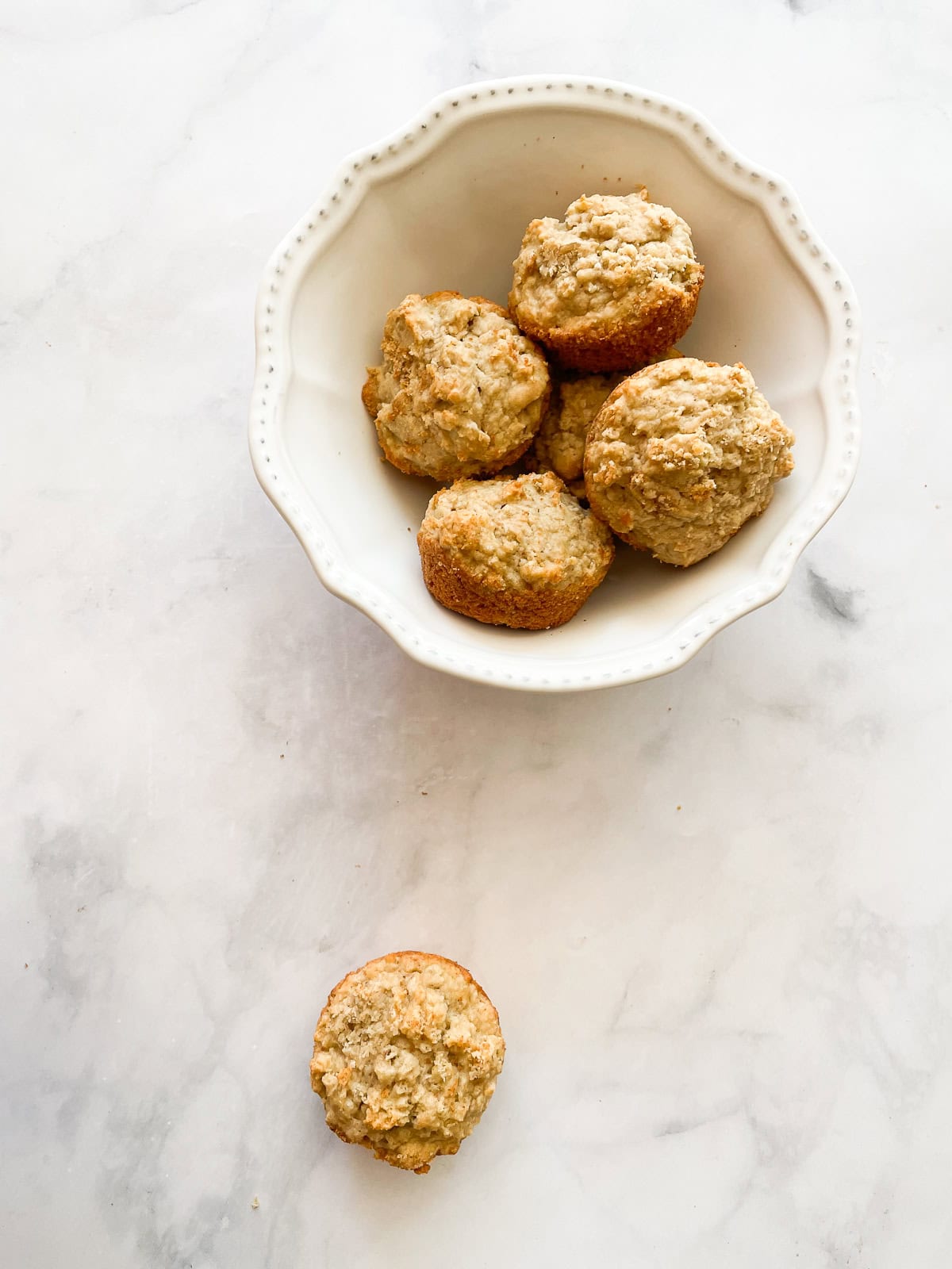 A leftover oatmeal muffin on a white counter with a bowl of muffins.