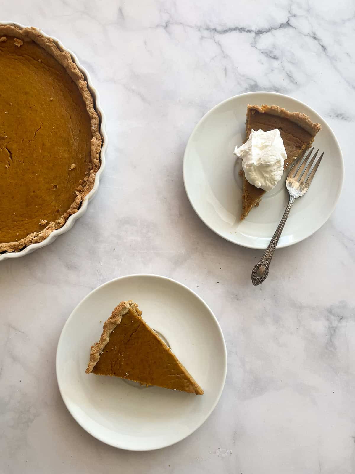 Pieces of maple pumpkin pie one topped with whipped cream on plates.