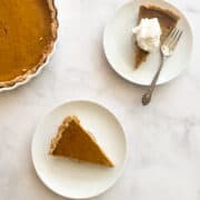 Pieces of maple pumpkin pie one topped with whipped cream on plates.