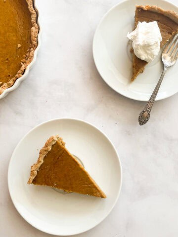 Pieces of maple pumpkin pie one topped with whipped cream on plates.