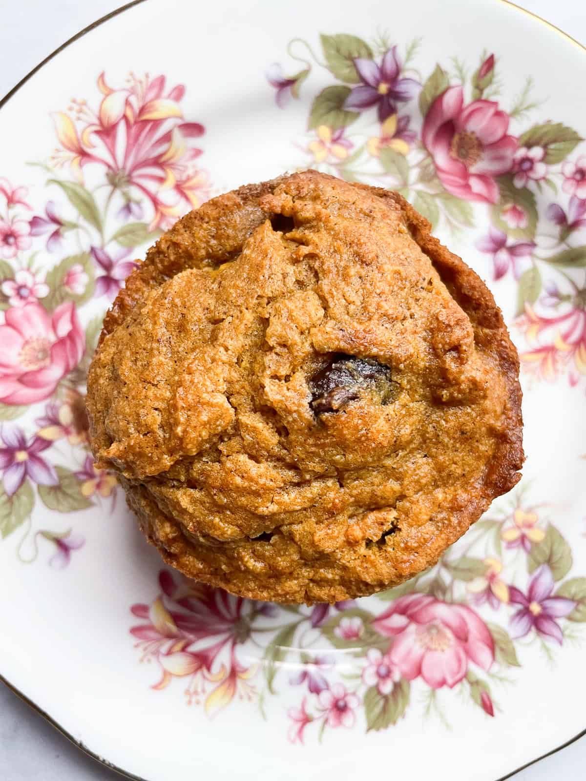 A chocolate chip oat flour pumpkin muffin on a flowered plate.