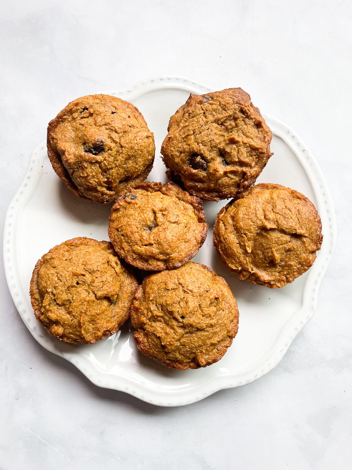 Six oat flour pumpkin muffins on a white plate.