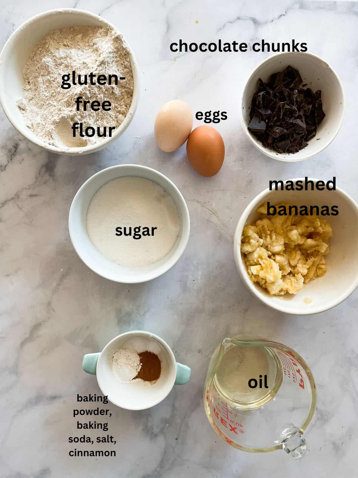 Ingredients for gluten free chocolate chunk banana muffins are portioned and text labeled.