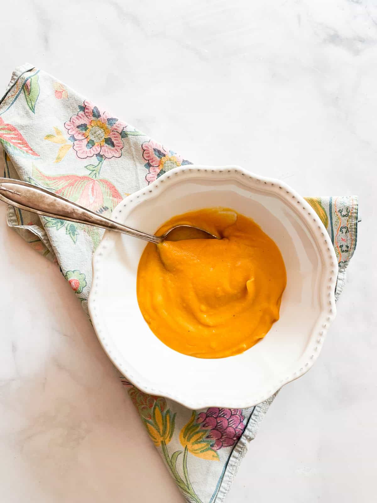 A white bowl of butternut squash with a spoon on a napkin.