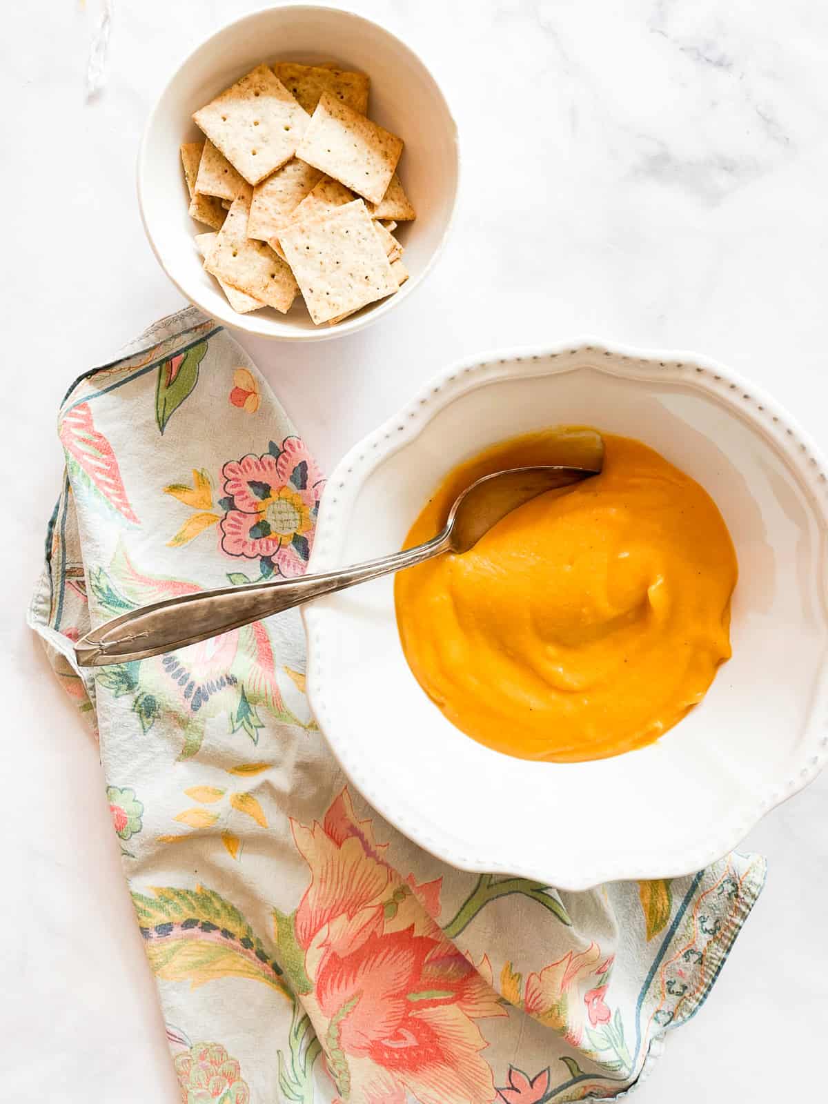 A bowl of crackers and a bowl of butternut squash soup.