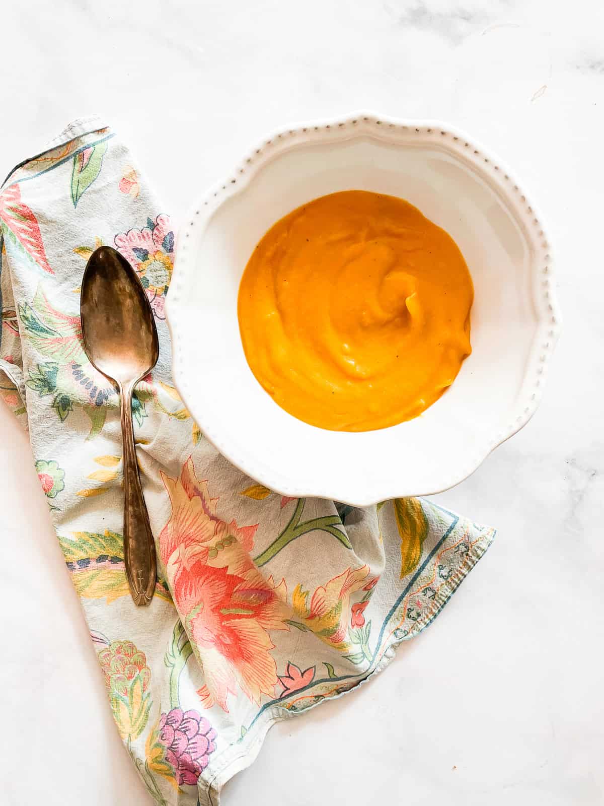 A bowl of butternut squash soup on a napkin with a spoon.