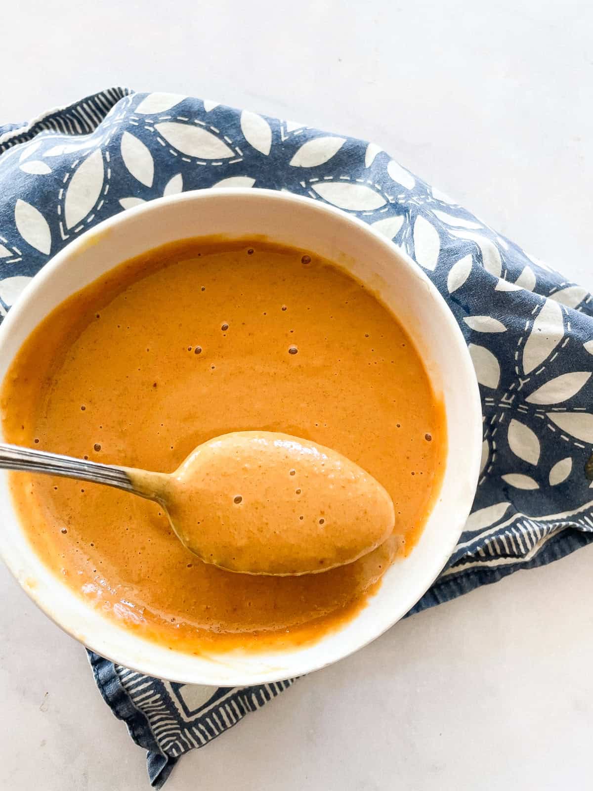 A spoonful of ginger peanut sauce above a bowl of sauce.