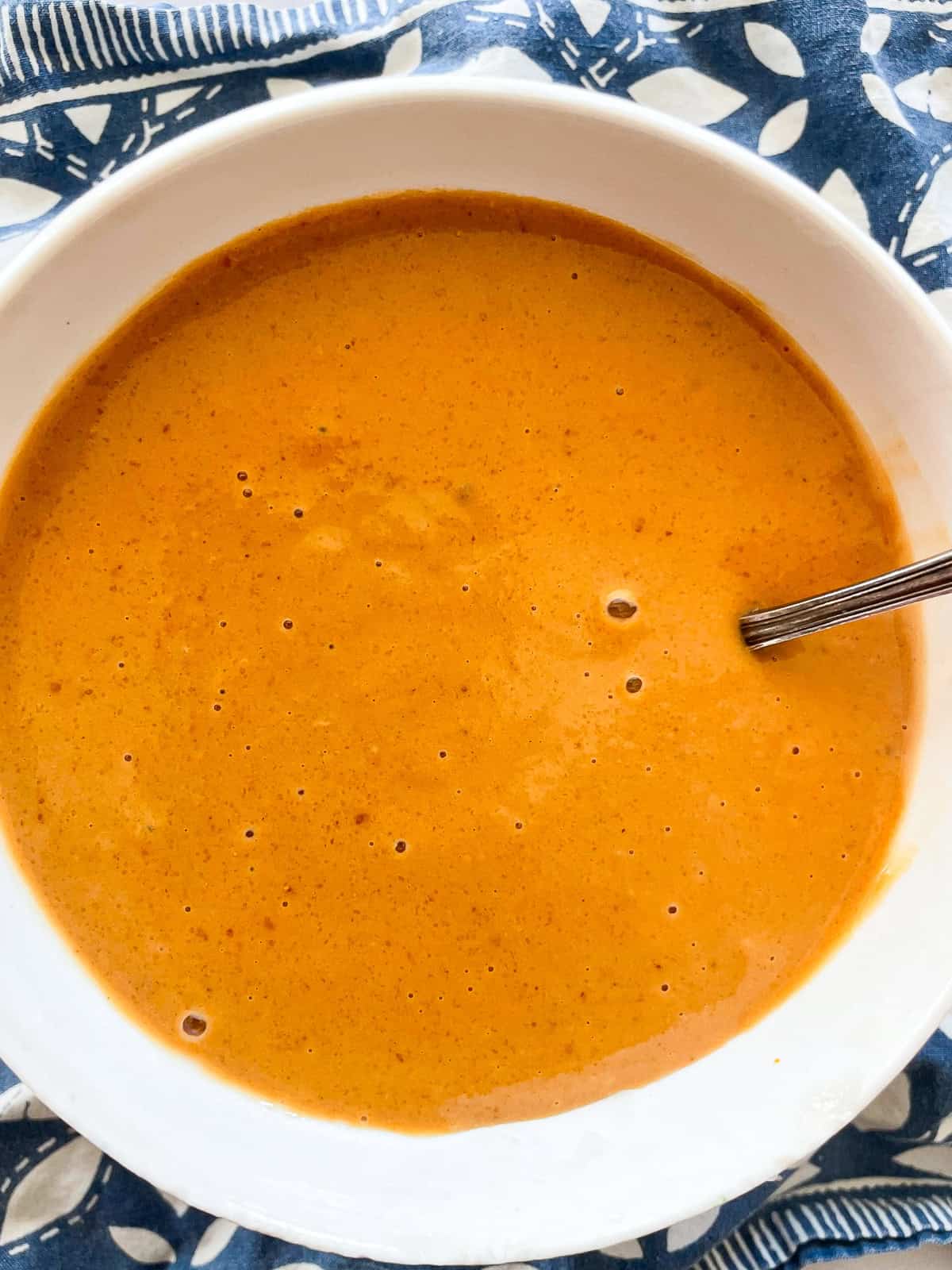 A spoon sticks out of a bowl of ginger peanut sauce.