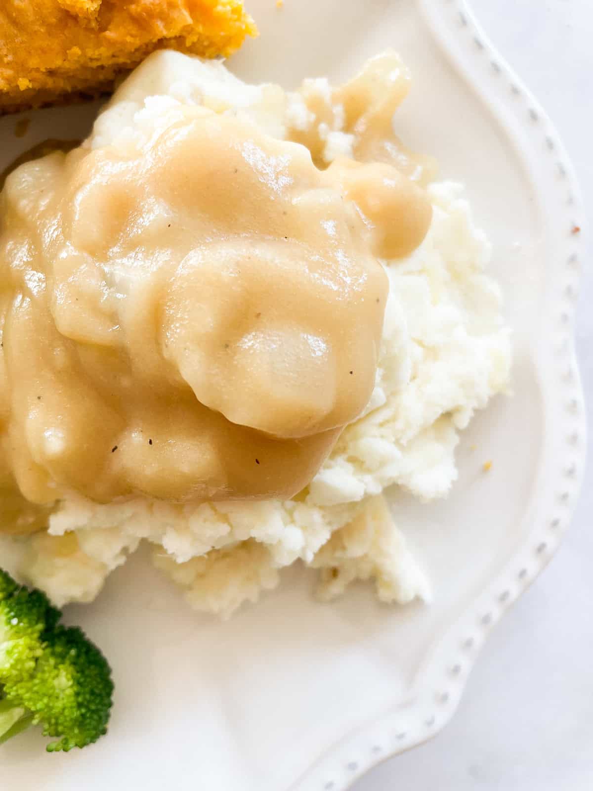 Easy gluten free gravy is an essential addition to the holiday table! Try this luxurious gravy on mashed potatoes, turkey, vegetarian dishes, and more. Mashed potatoes topped with gluten free gravy.