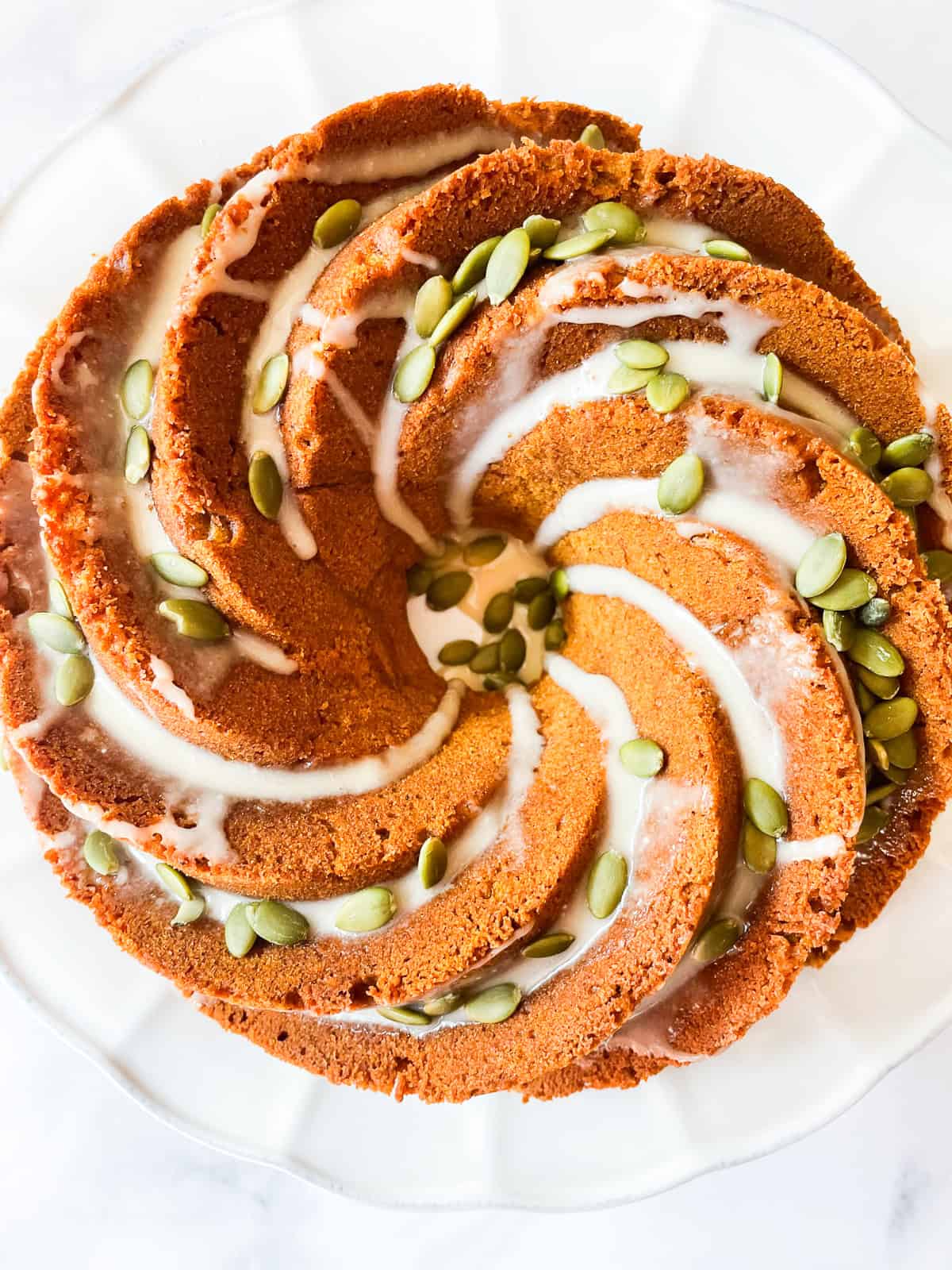 Glaze and pumpkin seeds on the top of a gluten free pumpkin bundt cake.