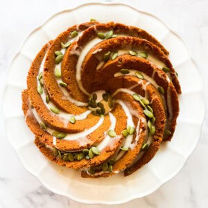 A gluten free pumpkin bundt cake topped with maple glaze and pumpkin seeds.