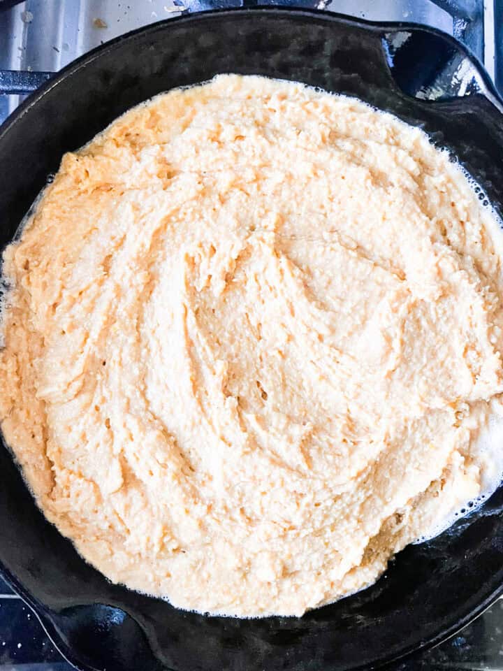 Pumpkin cornbread batter is added to a hot cast iron pan.