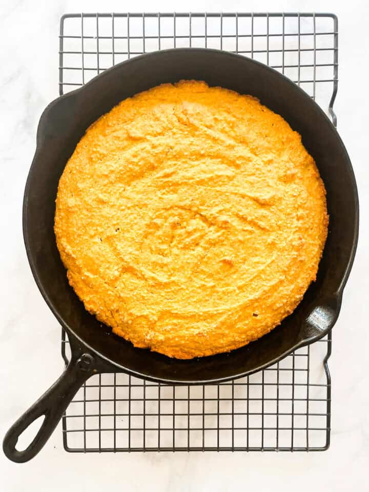 Pumpkin cornbread in a cast iron pan cools on a rack.