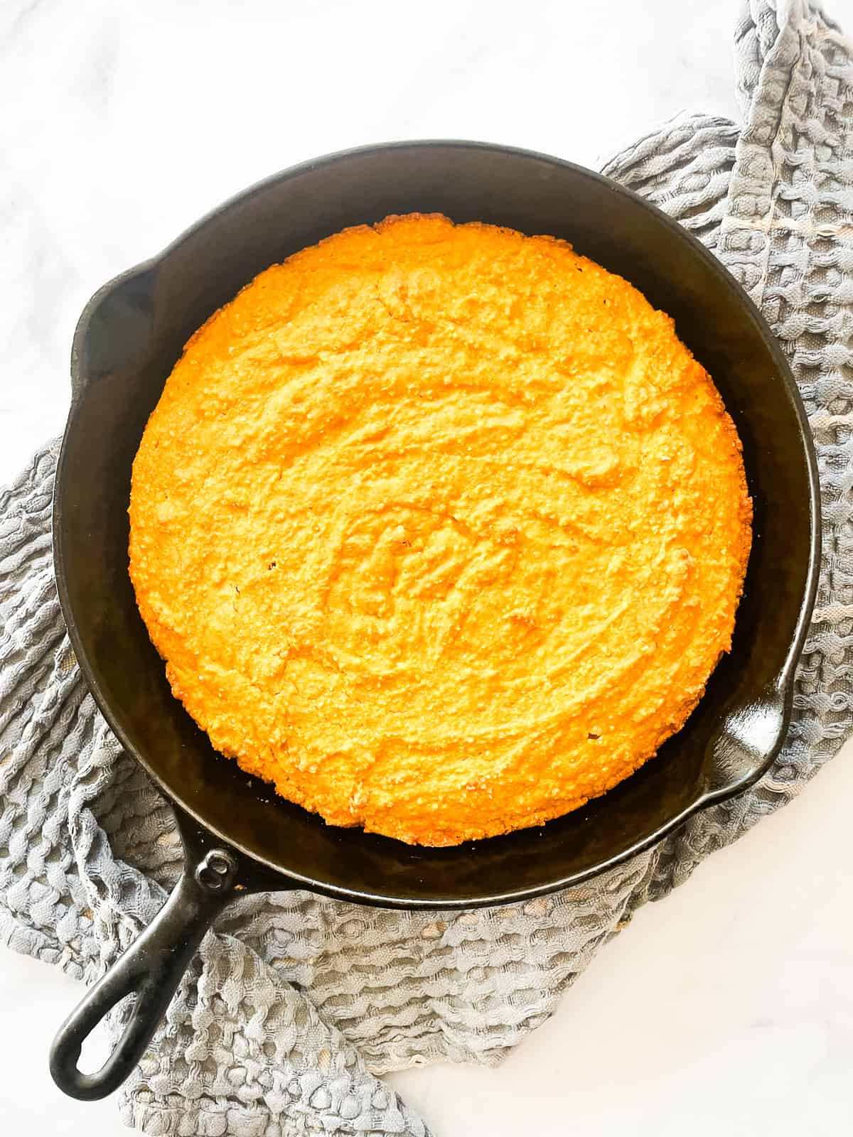 A cast iron pan of baked pumpkin cornbread on a blue towel.