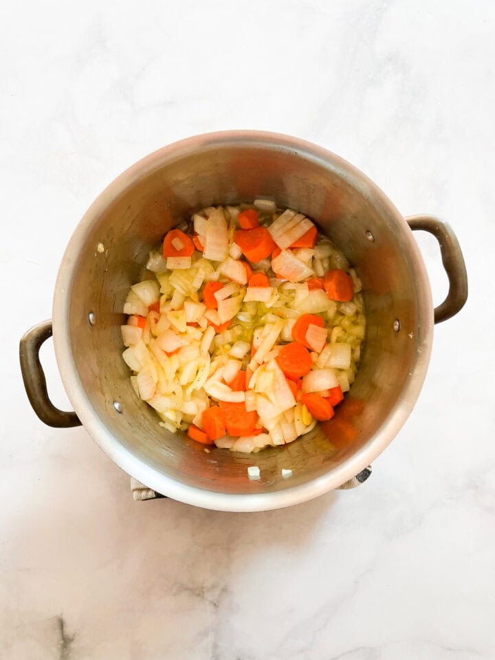 Carrots, onion, and garlic cook in a pot.