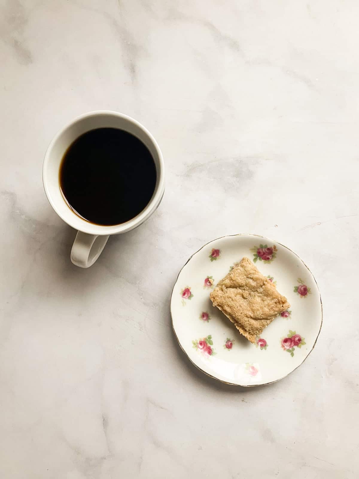 A square of maple shortbread on a small plate next to a cup of coffee.